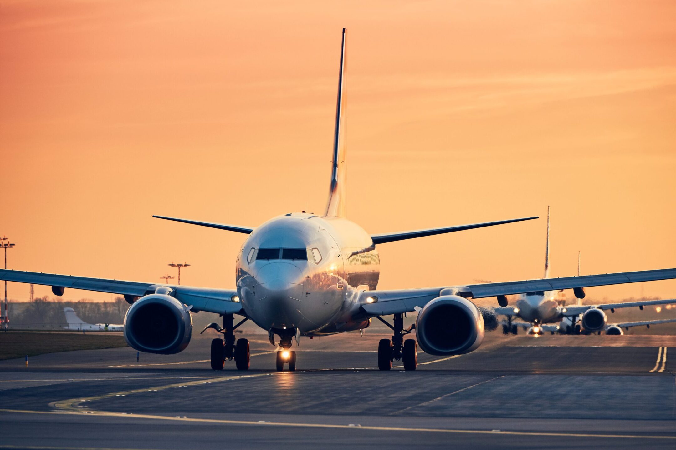 Airplanes in row taxiing to runway for take off. Traffic at busy airpot at sunset.